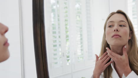 Biracial-woman-touching-her-face-looking-in-mirror-in-bathroom,-slow-motion