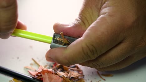 images de mains affûtant lentement un crayon et des crayons de couleur avec un taille-crayon en coin