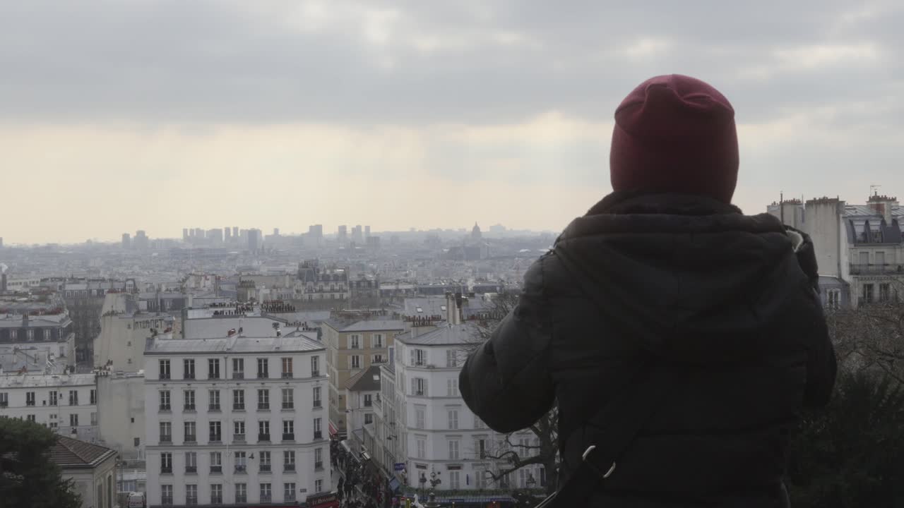 mujer con ropa cálida observando la ciudad de parís desde un techo en un día nublado