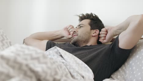 Sleepy-man-yawning-on-bed-in-morning.-Handsome-guy-stretching-in-bedroom.