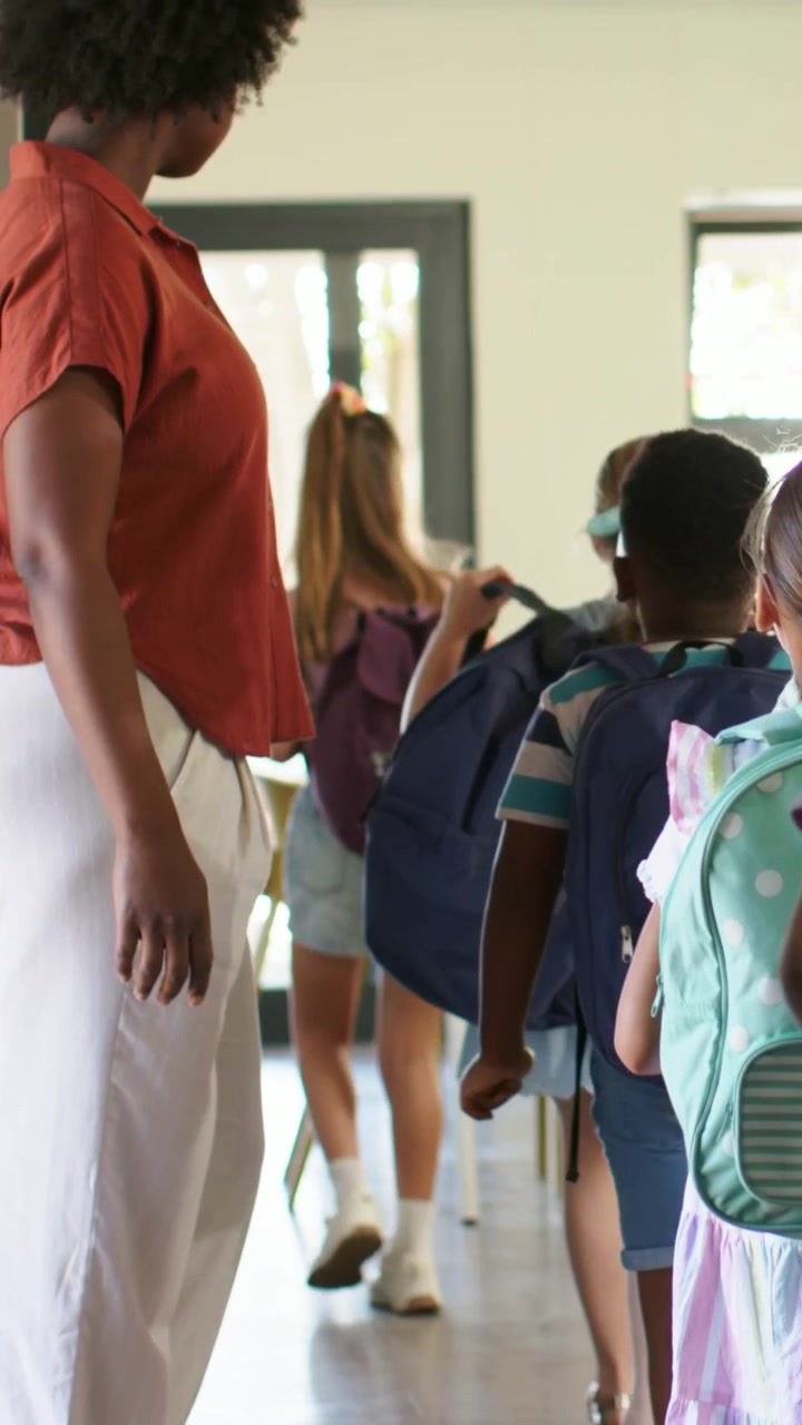 Vertical video: Walking on staff cue, kids going into class with bags, rust-top white-pants guiding