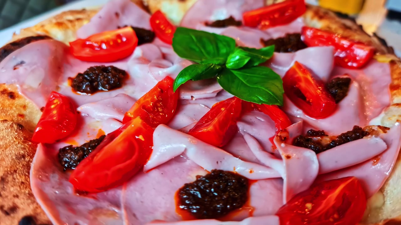 Uma deliciosa pizza artesanal gira lentamente, mostrando presunto, tomates e manjericão fresco.