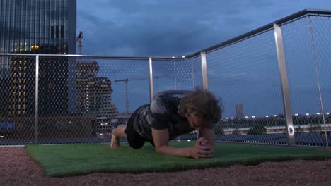 Guy-with-long-hair-is-doing-Plank-on-a-Terrace-with-the-viennese-Skyline-in-the-back-in-the-evening,-4K,-Timelapse