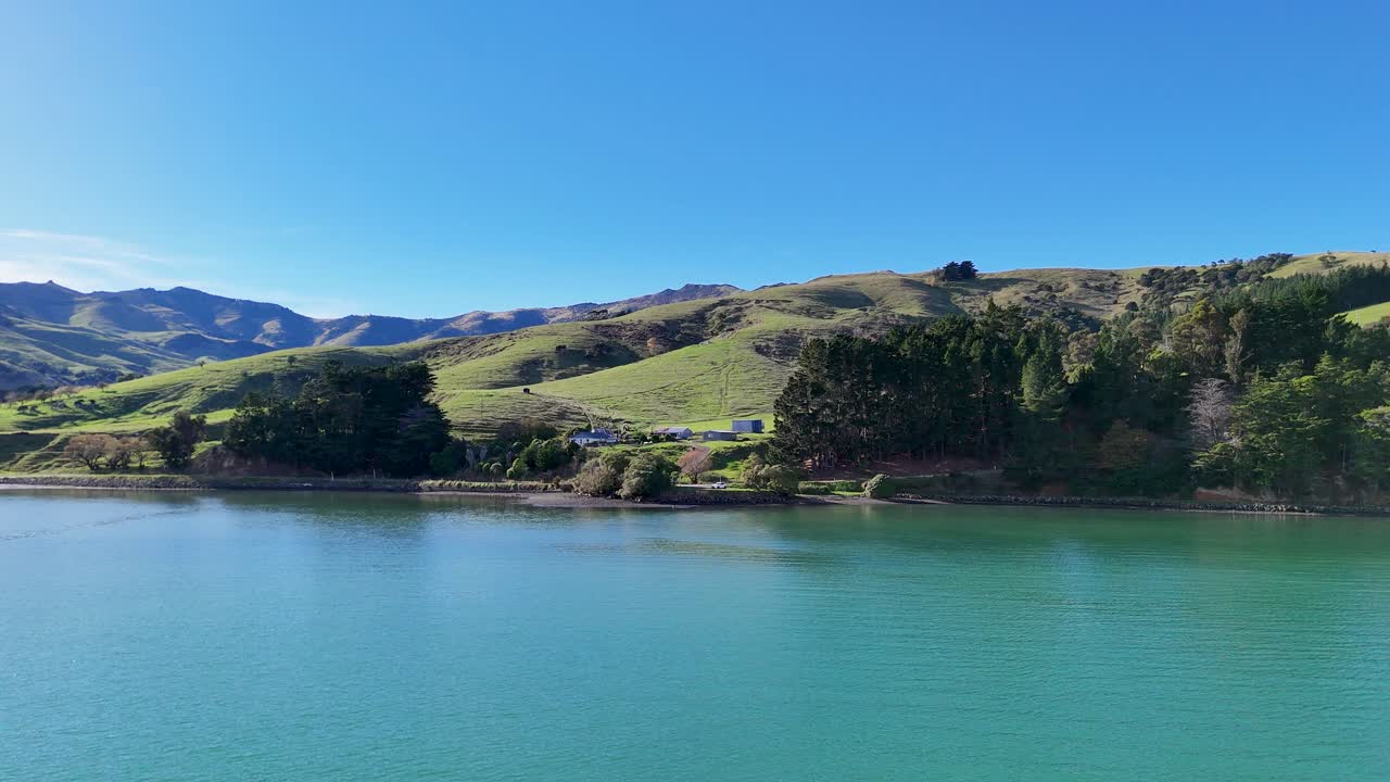 Aerial footage of Akaroa's serene lake and rolling hills under clear blue skies