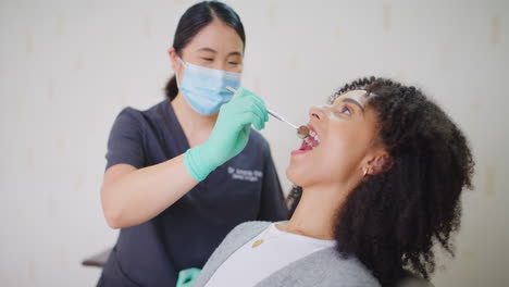 Dentist-with-face-mask-checking-teeth-of-a-female