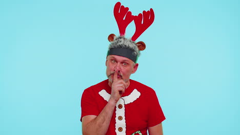 Man-wears-red-Christmas-t-shirt-presses-index-finger-to-lips-makes-silence-gesture-sign,-secret