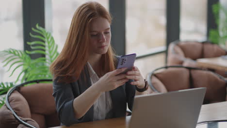 beautiful young business woman using phone in office. woman using a smartphone and leaning on a window texting sending emails planning meetings networking online browsing messages on mobile phone