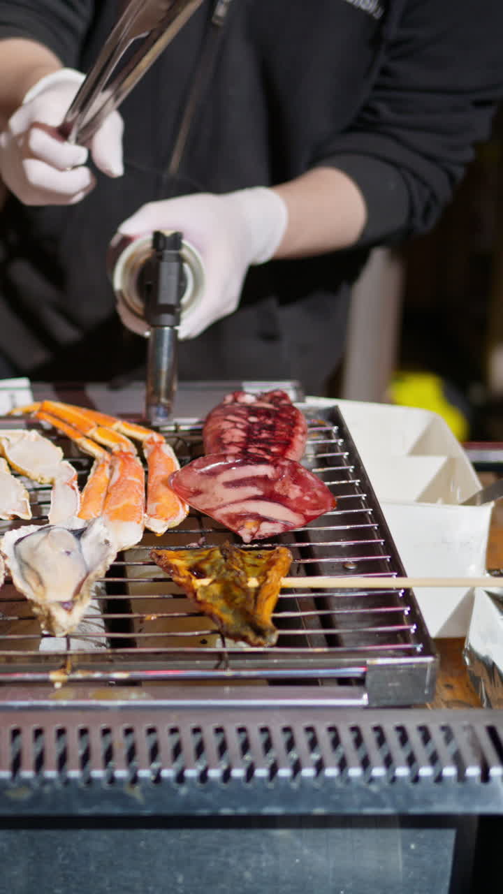 Close up of different types of seafood being grilled at the Tsukiji Fish Market in Chuo, Japan. Vertical