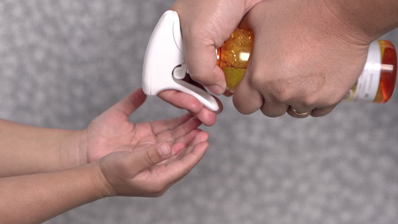 Mother sprays hand sanitizer on toddler for disinfection or cleaning