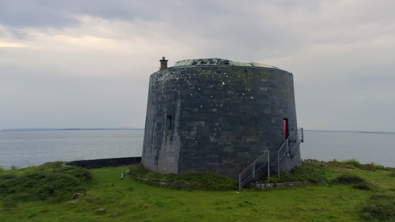 Trucking shot pans right around Aughinish Martello Tower at twilight overlooking Galway Bay
