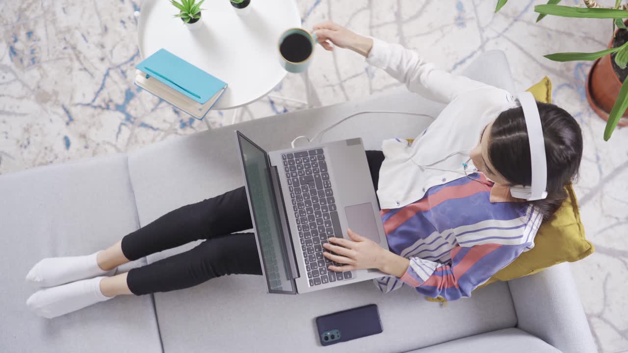 mujer joven sentada en el sofá en la sala de estar en casa y usando su computadora portátil.