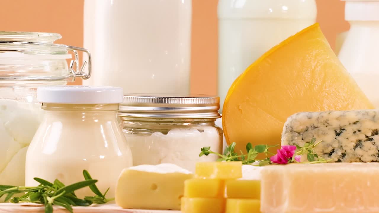 A variety of cheeses and dairy jars arranged neatly against a warm orange backdrop.