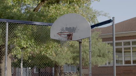 low angle view of an old basketball hoop and backboard against a fence on an elementary school playground