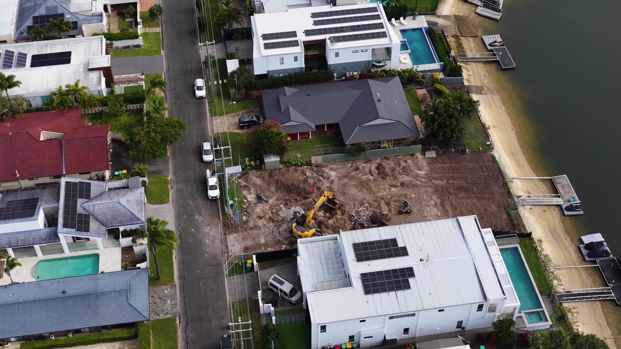 High-angle drone shot of luxury canal homes and an active excavator on a dirt lot.