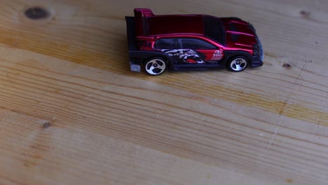 Red-toy-car-on-a-wooden-board-with-dark-background