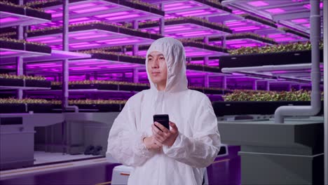 asian male scientist using smartphone and look around while standing in vertical farm