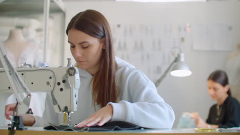 Dressmaker-sewing-clothes.-Fashion-designer-sewing-new-model-of-clothes.-Seamstress-woman-works-on-sewing-machine-in-tailoring-workshop-business.-She-stitches-details-for-future-clothing.