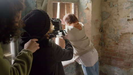 vista trasera de un camarógrafo grabando la escena de una chica tratando de escapar por la ventana de un edificio en ruinas