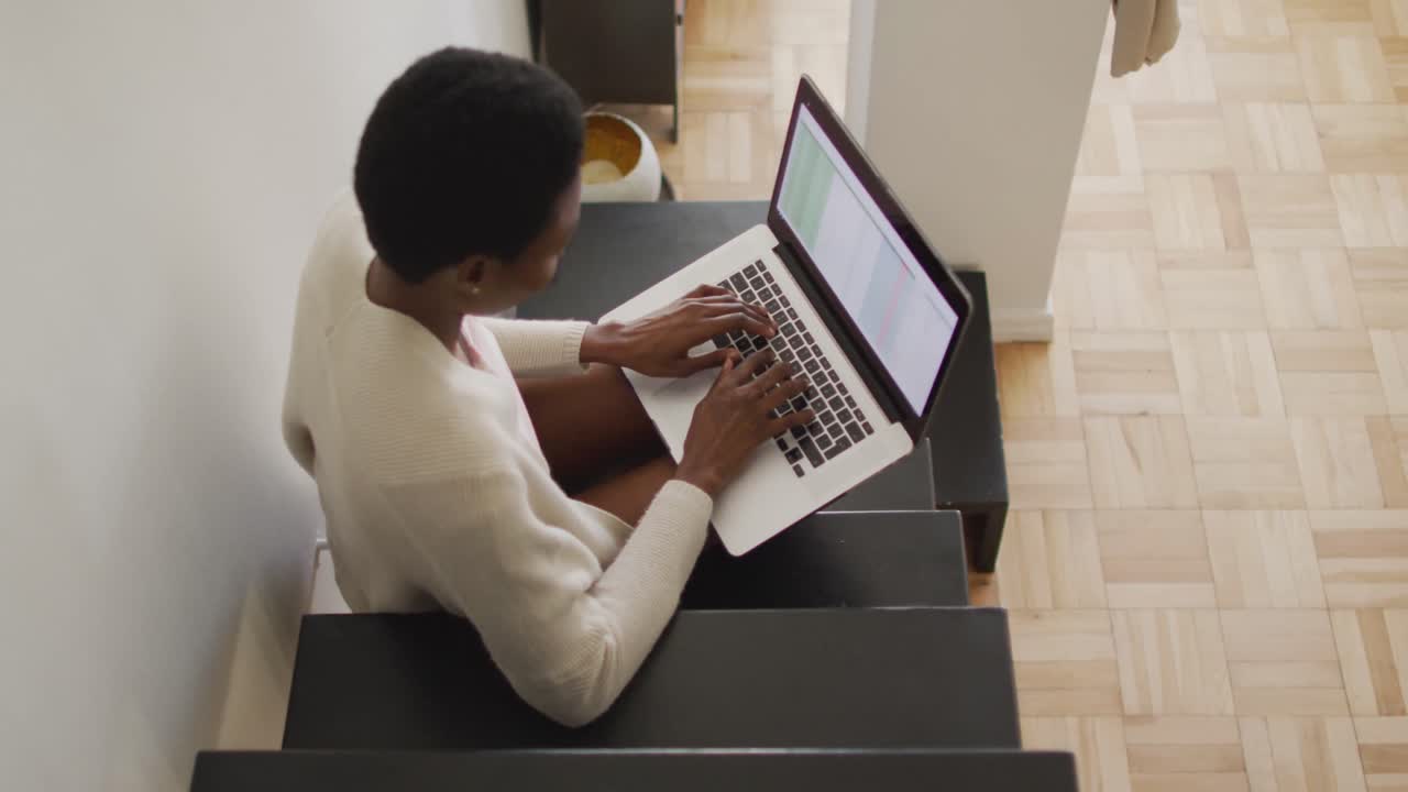 Happy african american woman sitting on stairs, using laptop
