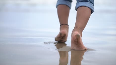 Siguiendo-Los-Pies-De-Un-Bebé-Indefinido-Caminando-En-La-Playa-Con-Sus-Padres-En-La-Tarde-Con-Olas-De-Mar-Salpicando-Sus-Piernas-Descalzas,-Cámara-Lenta