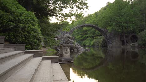 Puente-Del-Diablo-Rakotzbrucke-Formando-Un-Círculo-Perfecto-Con-El-Reflejo-En-El-Agua-En-El-Lago-Rakotz-Rodeado-Por-Un-Denso-Bosque,-Gablenz,-Alemania