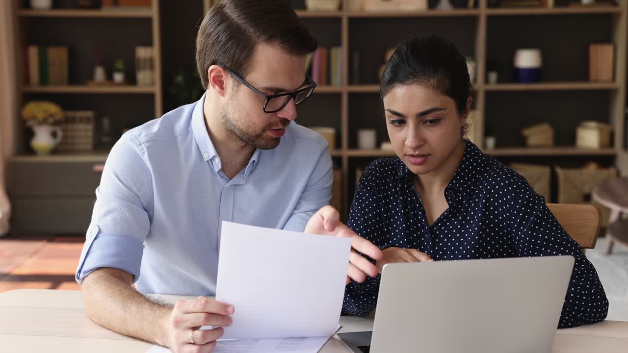 dos colegas multiétnicos se sientan en el escritorio usan la computadora portátil discuten el papeleo