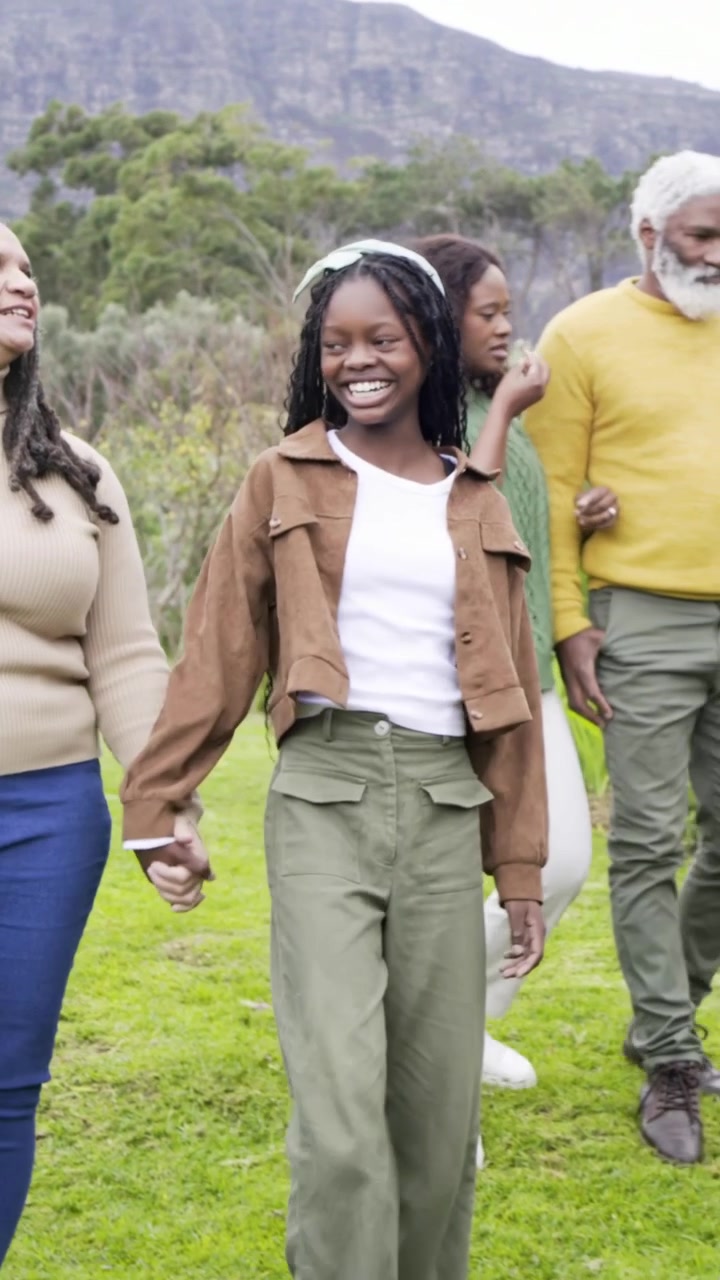 Vertical video: Walking child in brown jacket holding adult hand on lawn, camera tracking family