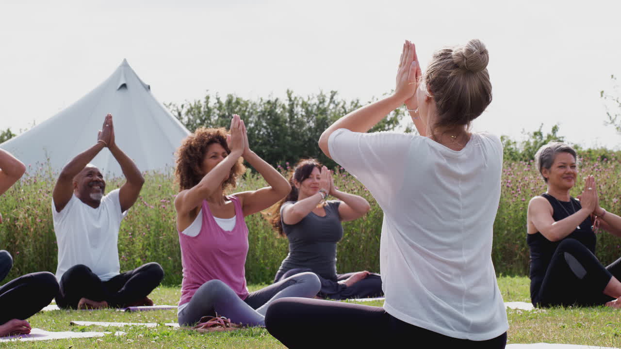 maestra liderando un grupo de hombres y mujeres maduros en clase en un retiro de yoga al aire libre