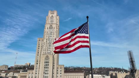 american flag waving in front of pitt cathedral of learning and blue sky