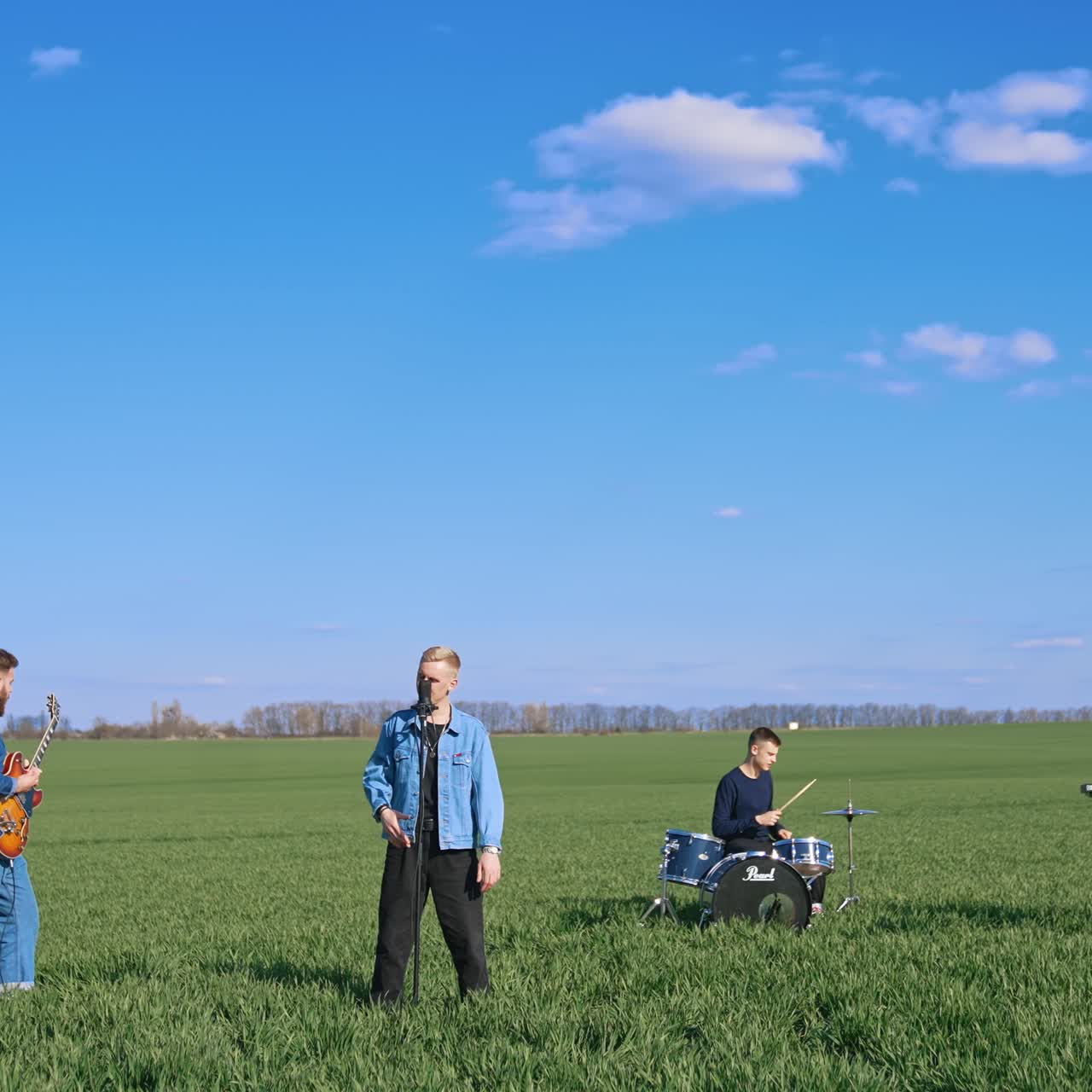 Young musical band giving a concert on field. Friends perform music with musical instruments under blue sky. Outdoor entertainment
