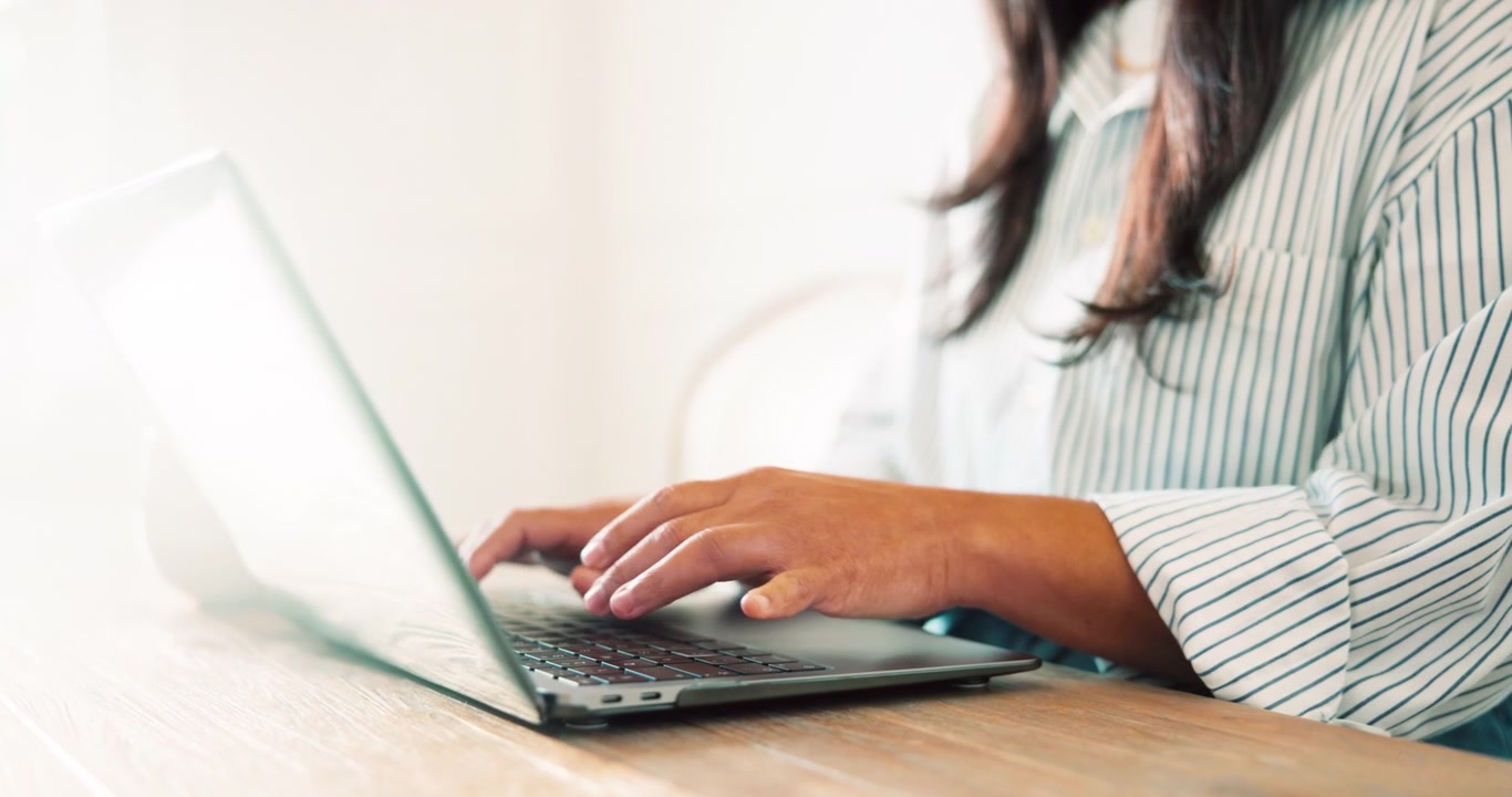Mulher abrindo um laptop e digitando em uma mesa