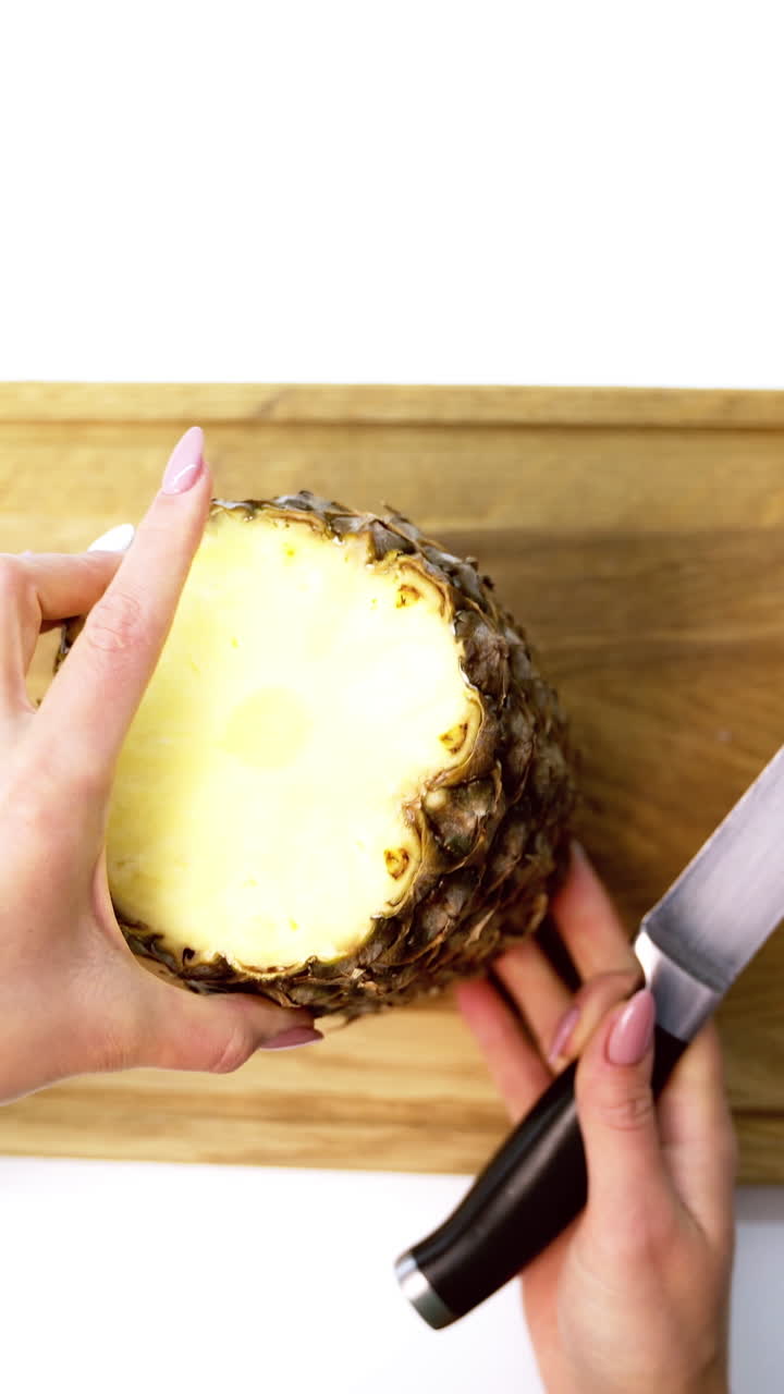 Tropical fruit on a board. Female's hands cleaning fresh pineapple with a knife on a cutting board. Top view. Vertical video