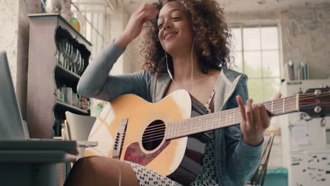 attractive mixed race young girl learning to play guitar using laptop computer