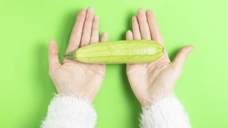 video 4k ripe young zucchini lies on the palms of a girl in a white fluffy sweater moves on a green background