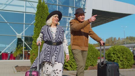 elderly husband wife retirees tourists go to airport terminal for boarding with luggage on wheels