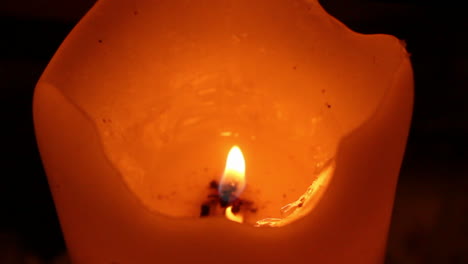 angled view of a yellow, orange and red candle with a litted shaky flame and melted wax on dark background