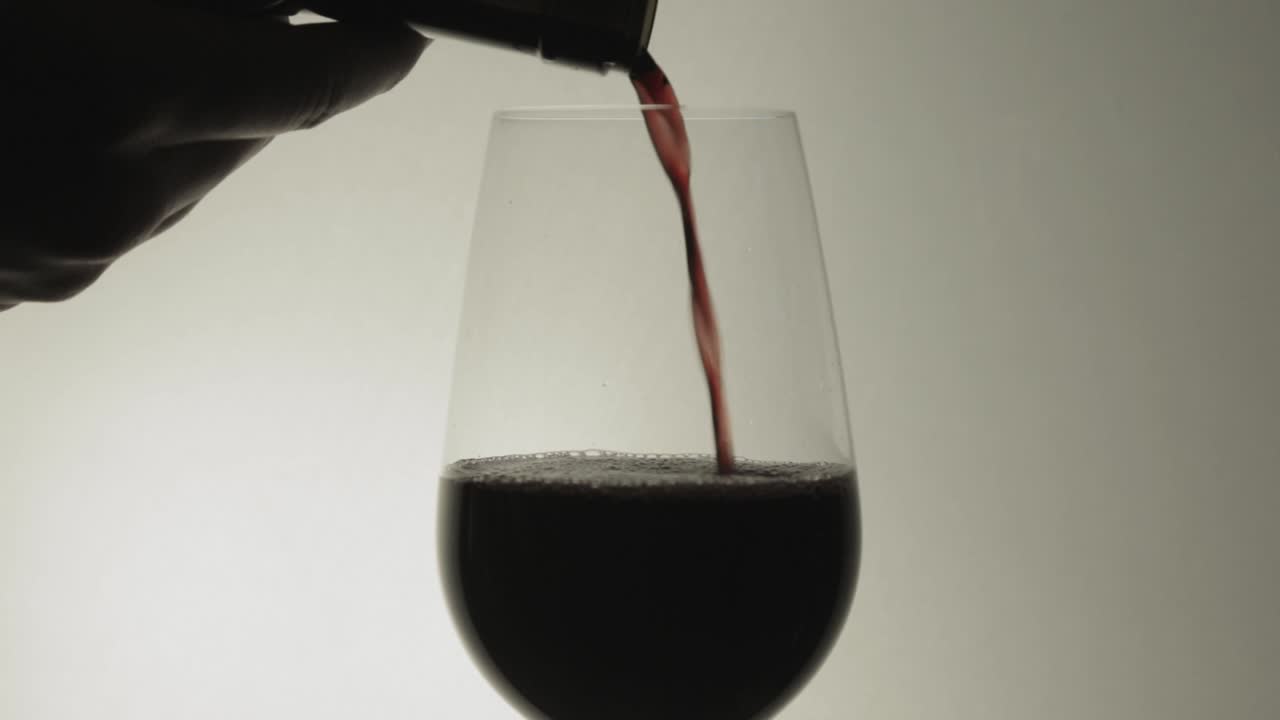 Pouring red wine into a transparent glass with white background - Close up