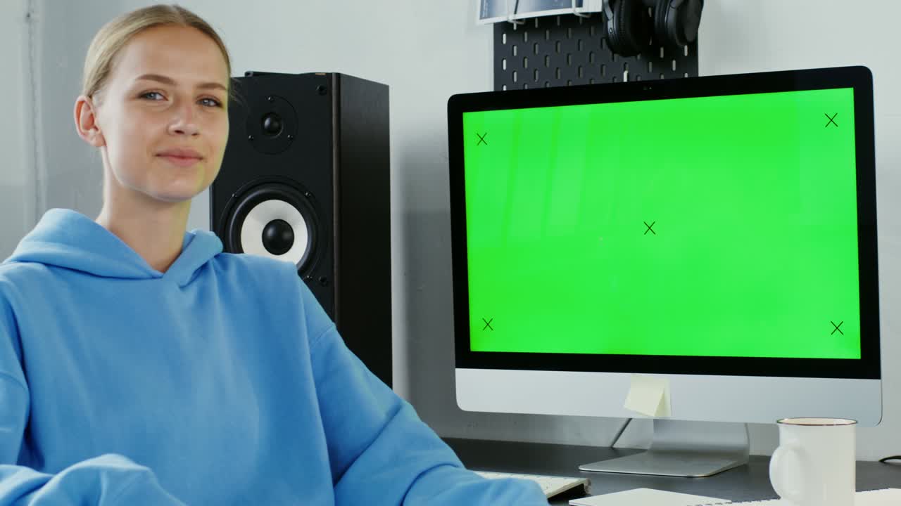 joven sonriendo mirando a la cámara sentada frente a un monitor verde