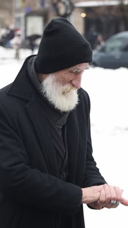 an elderly man with a white beard wearing a black hat and coat in winter