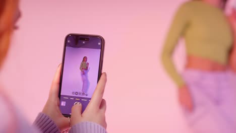 fotografía de estudio de una mujer tomando una foto de una amiga bailando en un teléfono móvil contra un fondo rosa 1
