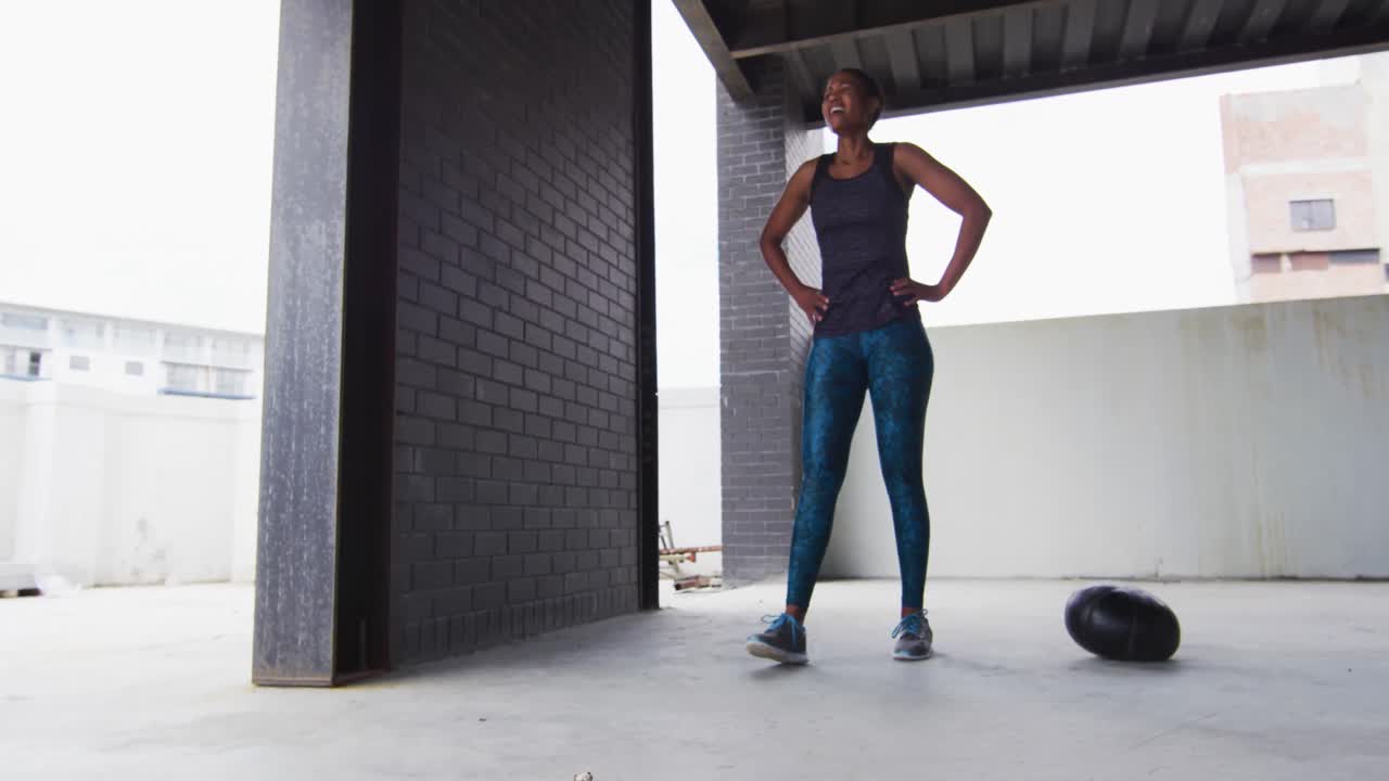 African american woman resting after exercising with medicine ball in an empty urban building