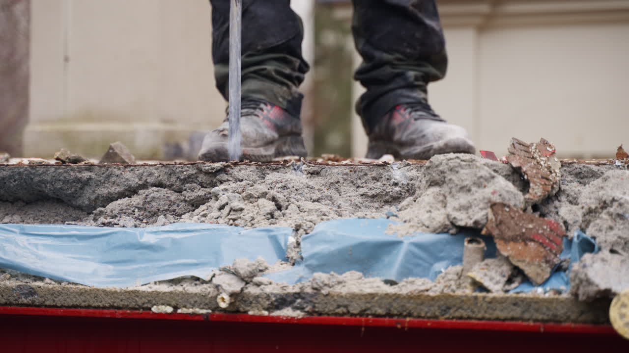 Un operaio in un cantiere edile che demolisce pavimentazione in asfalto o cemento con un martello pneumatico, vista frontale