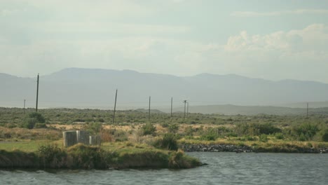 imágenes de teleobjetivo pacíficas de un estanque y postes de teléfono que van a lo lejos, grandes nubes y montañas se ven a lo lejos, con artemisa y otras hierbas secas