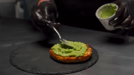 spreading avocado on hamburger bun chef at gourmet restaurant kitchen guacamole preparation recipe snack