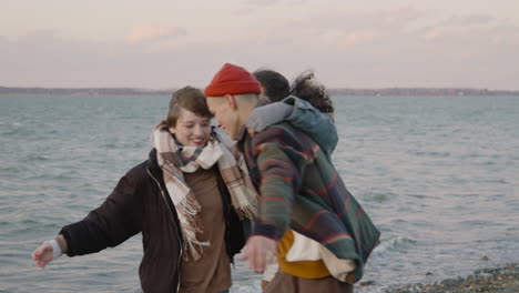 three friends in winter clothes hugging and smiling on a seashore on a windy day