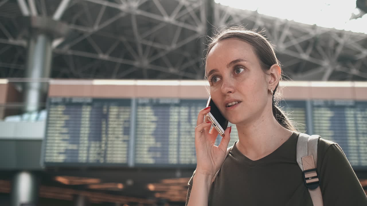A woman traveler with a backpack at the airport discusses the delay of his flight on the phone. Transfer and delay of departure from the airport