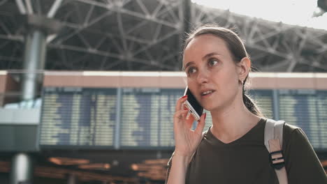una mujer viajera con una mochila en el aeropuerto discute el retraso de su vuelo por teléfono. transferencia y retraso de la salida del aeropuerto