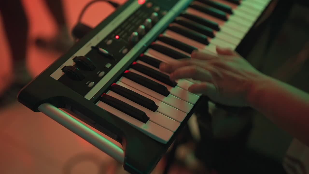 Musiker spelar synthesizer under ett liveframträdande, händer trycker ner tangenter och skapar elektronisk musik i en närbild, högvinkelvy, levande scenbelysning