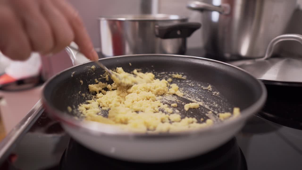 Handheld close up shot of person frying something on pan in home kitchen
