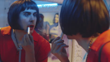 transgender man putting on red lipstick in nightclub bathroom